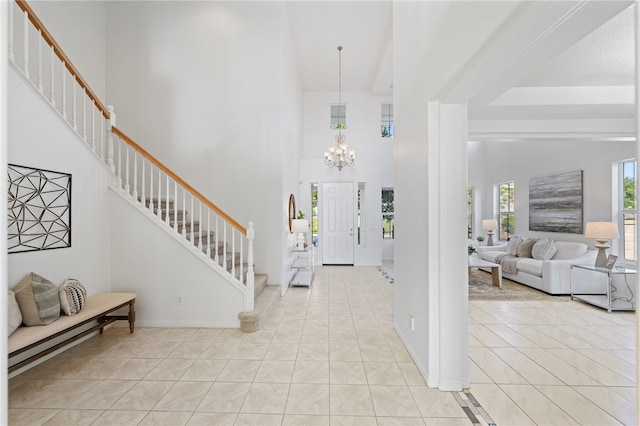 foyer with light tile patterned floors, a notable chandelier, a towering ceiling, and stairs