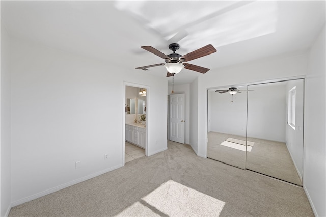 unfurnished bedroom featuring ceiling fan, connected bathroom, light carpet, baseboards, and a closet