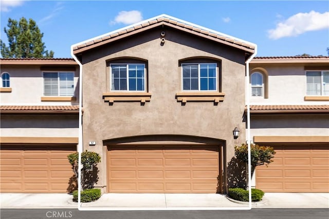 mediterranean / spanish house with stucco siding, an attached garage, and a tile roof