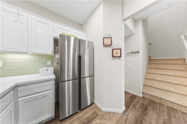 kitchen with light wood finished floors, freestanding refrigerator, light countertops, white cabinets, and tasteful backsplash