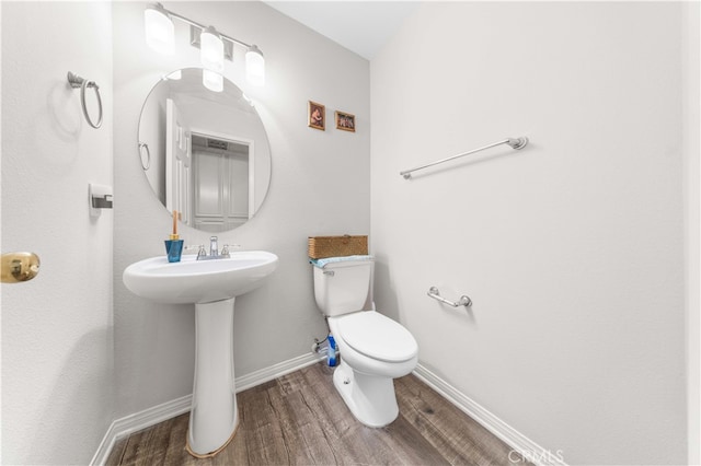 half bath featuring a sink, baseboards, toilet, and wood finished floors