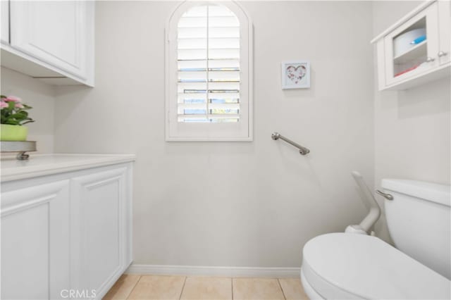 half bath featuring tile patterned floors, toilet, vanity, and baseboards