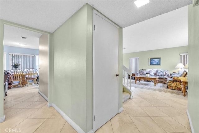 hallway with light tile patterned floors, baseboards, stairway, and a textured ceiling