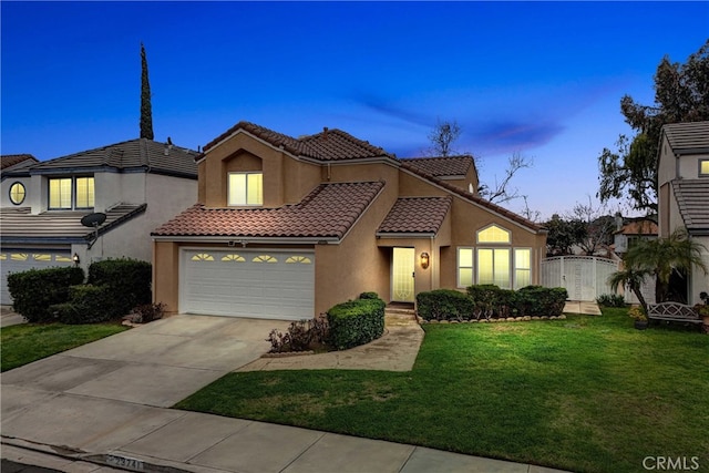 mediterranean / spanish home with an attached garage, a tile roof, driveway, stucco siding, and a front yard