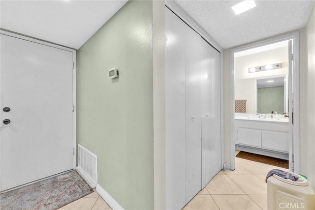 hall featuring visible vents, a textured ceiling, baseboards, and light tile patterned flooring