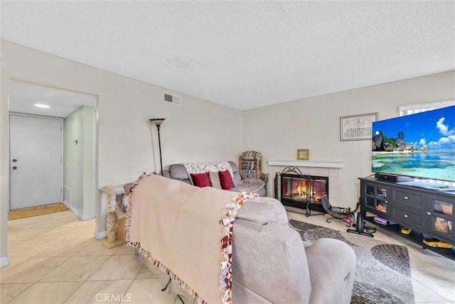 living area featuring a textured ceiling, light tile patterned flooring, a tiled fireplace, and visible vents