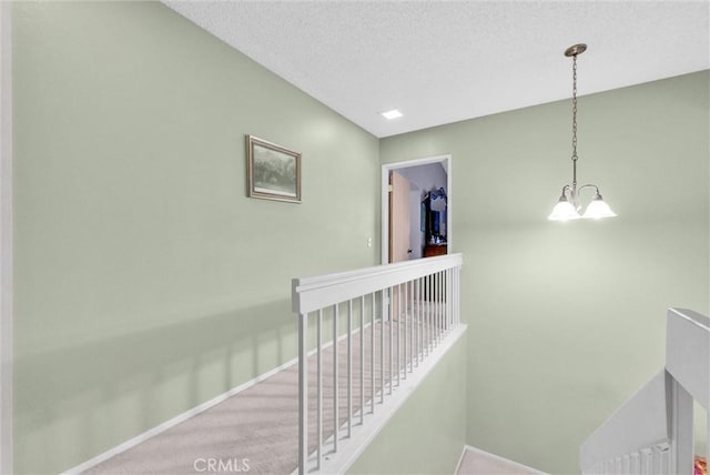 hall featuring baseboards, a textured ceiling, an upstairs landing, and an inviting chandelier