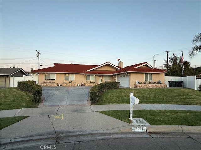 ranch-style home featuring stucco siding, concrete driveway, a front yard, fence, and a garage