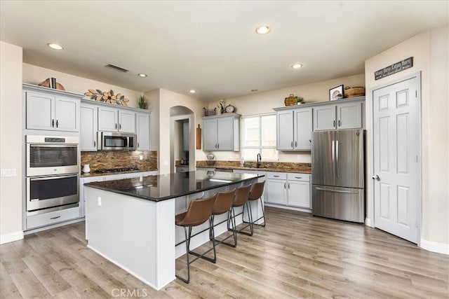 kitchen featuring arched walkways, light wood-style flooring, stainless steel appliances, a sink, and a kitchen island