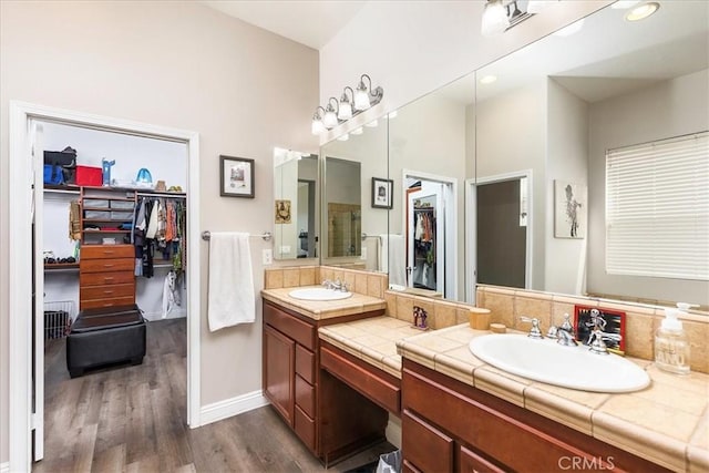 bathroom featuring double vanity, a walk in closet, a sink, and wood finished floors