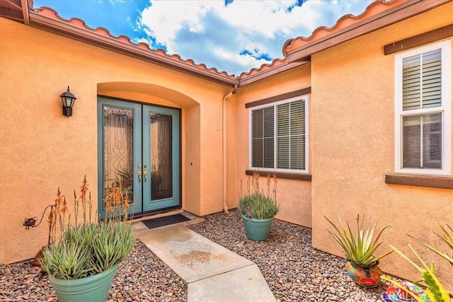 view of exterior entry with stucco siding, a tile roof, and french doors