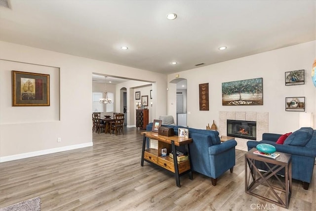 living room with arched walkways, light wood finished floors, recessed lighting, a tile fireplace, and baseboards