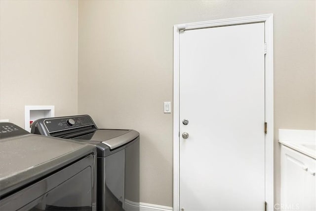 washroom featuring washing machine and clothes dryer, cabinet space, and baseboards