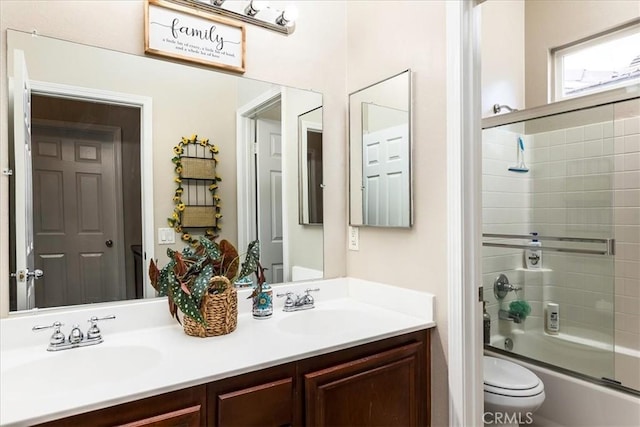 full bathroom with bath / shower combo with glass door, a sink, toilet, and double vanity