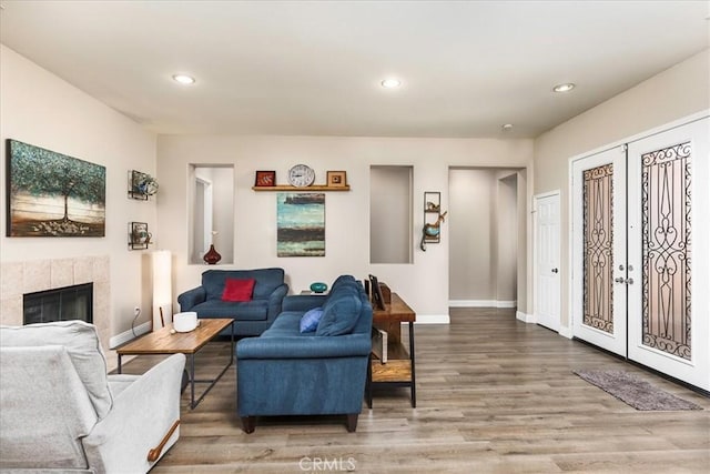 living area featuring a fireplace, baseboards, wood finished floors, and french doors