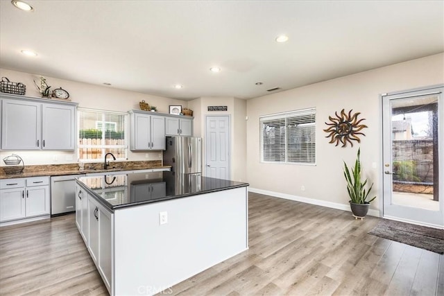 kitchen featuring light wood finished floors, stainless steel appliances, a sink, a kitchen island, and baseboards