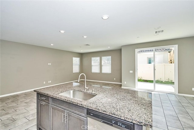 kitchen featuring visible vents, dishwasher, open floor plan, light stone countertops, and a sink