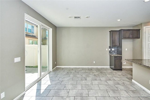 interior space with tasteful backsplash, visible vents, dark brown cabinetry, light stone countertops, and baseboards