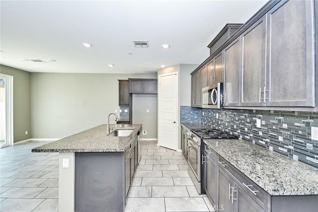 kitchen with light stone counters, visible vents, decorative backsplash, appliances with stainless steel finishes, and a sink