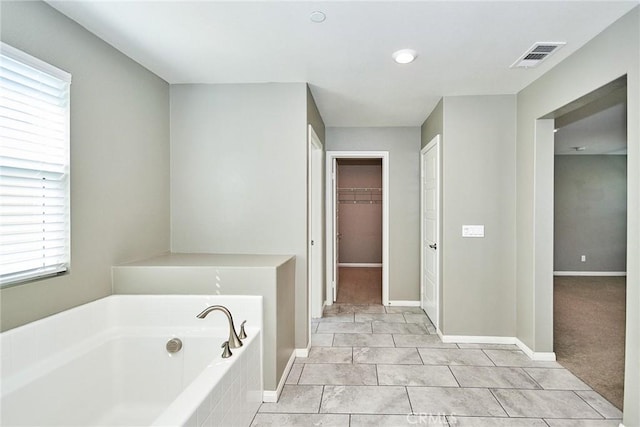 full bath featuring a spacious closet, a garden tub, visible vents, and baseboards