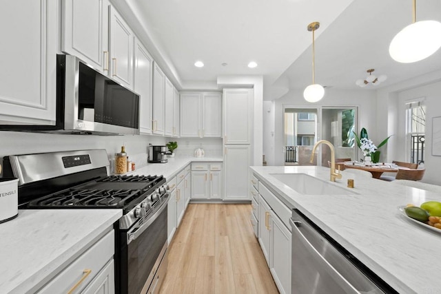 kitchen with white cabinets, hanging light fixtures, stainless steel appliances, light wood-style floors, and a sink