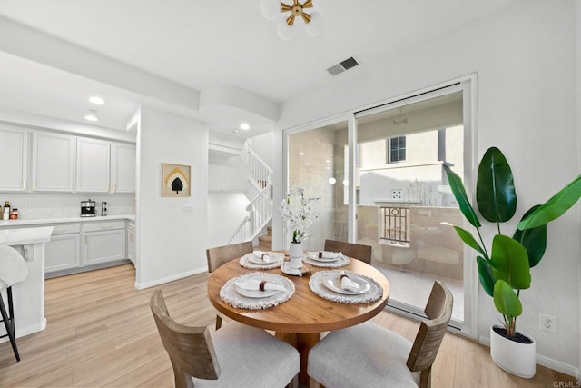 dining room featuring light wood-type flooring, stairway, baseboards, and visible vents