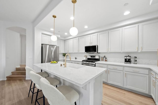 kitchen with light stone countertops, a kitchen island with sink, stainless steel appliances, light wood-style floors, and a sink