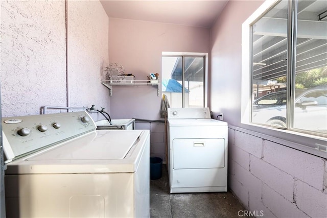 washroom with concrete block wall, laundry area, and separate washer and dryer