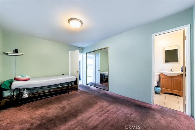 bedroom featuring ensuite bathroom, light tile patterned flooring, light carpet, a sink, and a closet