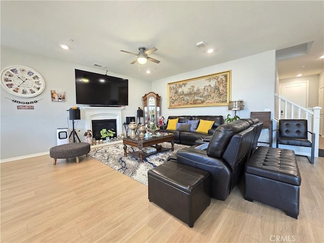 living area featuring a fireplace, visible vents, a ceiling fan, stairs, and light wood-style floors