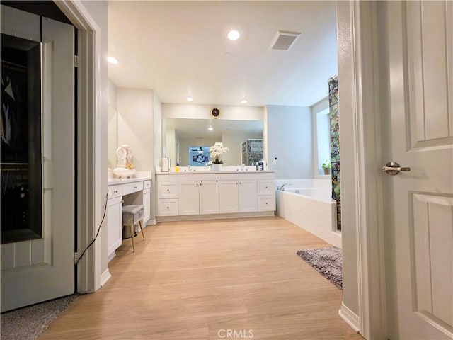 bathroom with recessed lighting, wood finished floors, vanity, visible vents, and a bath