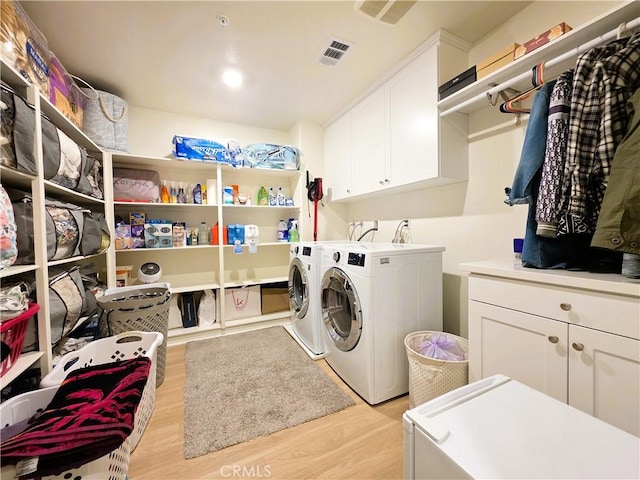 washroom with light wood-style flooring, visible vents, cabinet space, and washer and clothes dryer