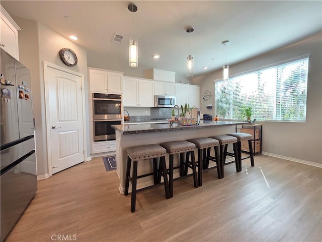 kitchen with white cabinets, decorative backsplash, appliances with stainless steel finishes, a kitchen breakfast bar, and light wood-type flooring