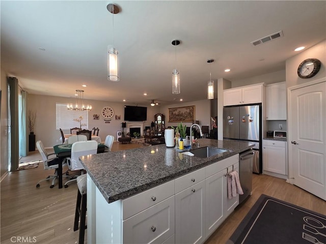 kitchen with a fireplace, a sink, white cabinets, light wood-style floors, and appliances with stainless steel finishes