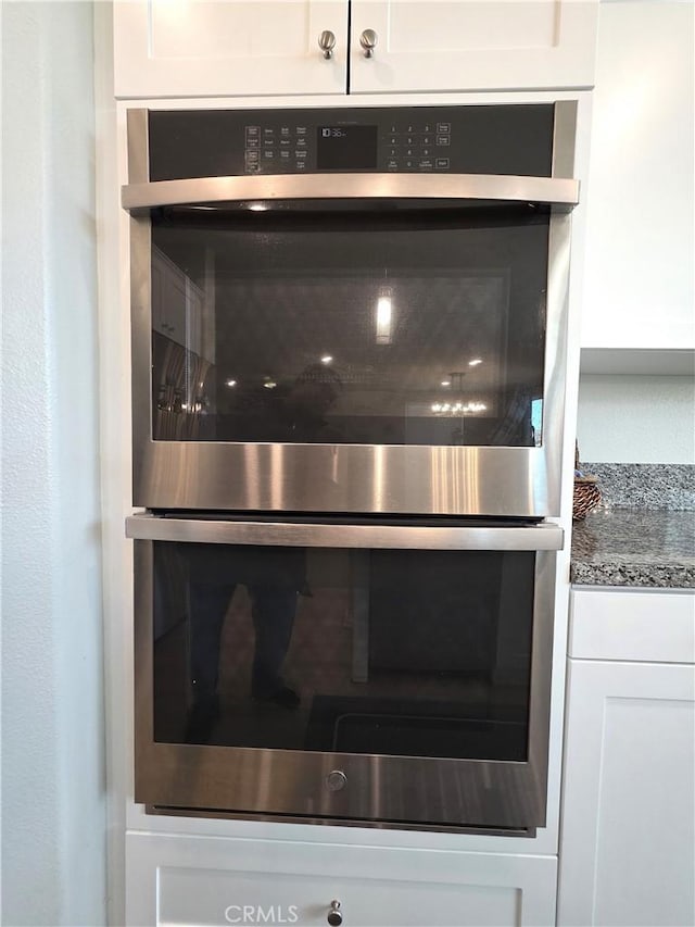 interior details featuring stainless steel double oven, stone counters, and white cabinetry