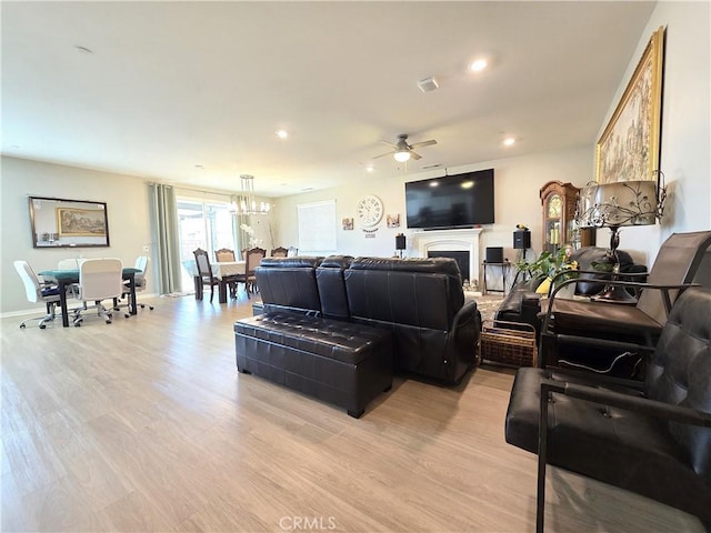 living area featuring ceiling fan with notable chandelier, recessed lighting, a fireplace, and light wood-style floors