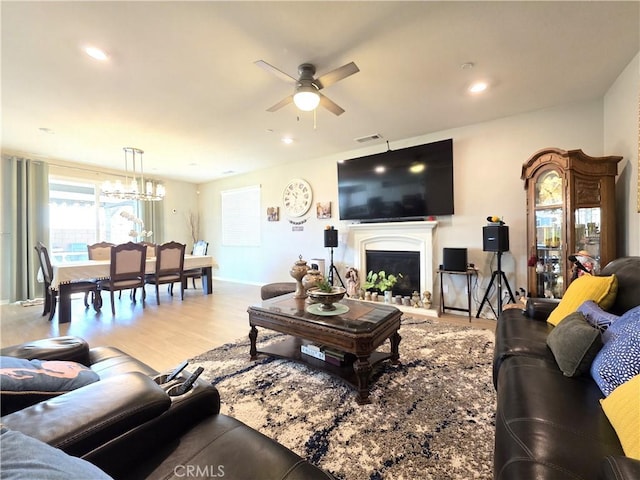 living room with visible vents, wood finished floors, ceiling fan with notable chandelier, a fireplace, and recessed lighting