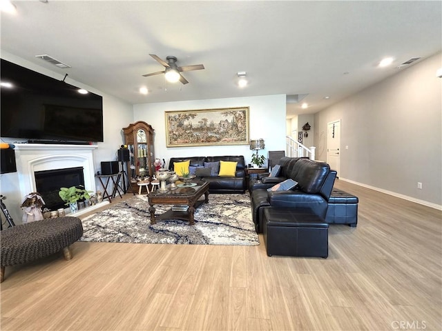 living area featuring a fireplace, wood finished floors, a ceiling fan, visible vents, and baseboards