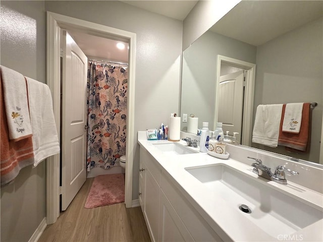 bathroom with toilet, double vanity, a sink, and wood finished floors