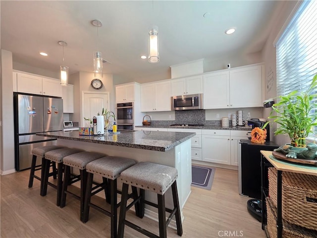 kitchen with dark stone countertops, stainless steel appliances, light wood-type flooring, white cabinetry, and backsplash