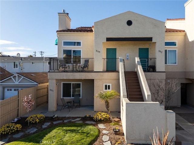 rear view of property with a tile roof, a chimney, fence, a patio area, and stucco siding