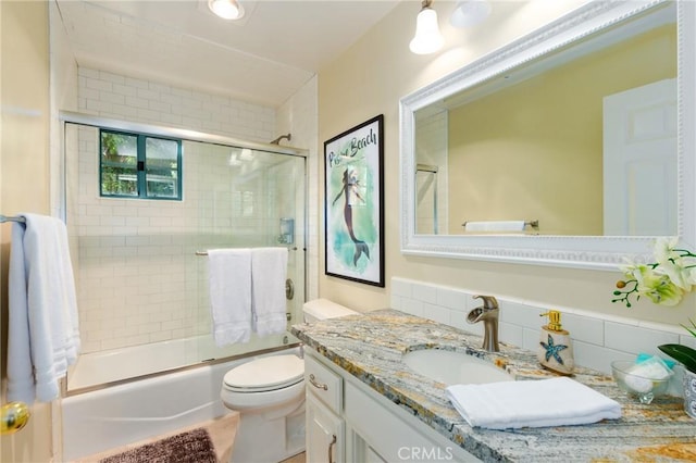 bathroom with tasteful backsplash, shower / bath combination with glass door, vanity, and toilet