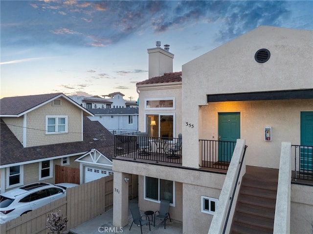 rear view of property featuring a balcony, a chimney, fence, a patio area, and stucco siding