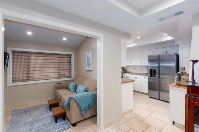 kitchen featuring stone tile floors, stainless steel fridge, visible vents, decorative backsplash, and white cabinetry