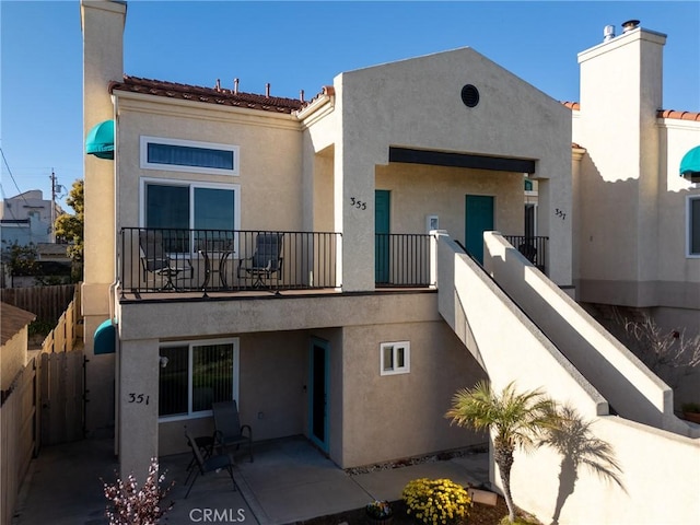 rear view of house featuring a patio area, fence, a balcony, and stucco siding