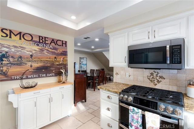 kitchen featuring stone tile floors, stainless steel appliances, recessed lighting, backsplash, and white cabinets