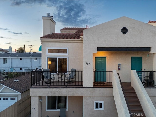 back of property at dusk featuring a tiled roof, a chimney, and stucco siding