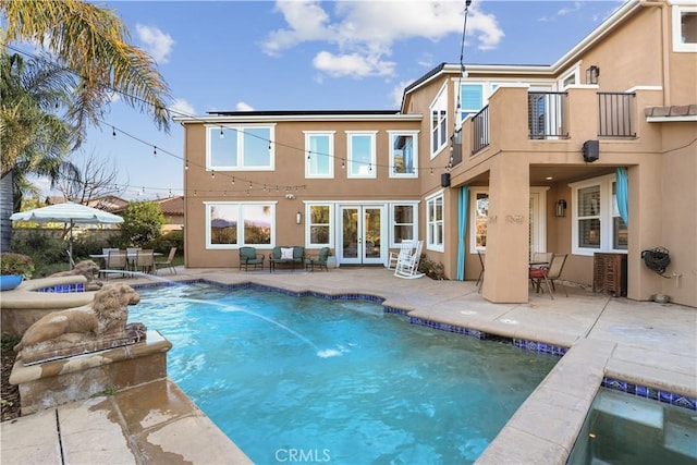 back of property with a fenced in pool, stucco siding, french doors, a balcony, and a patio