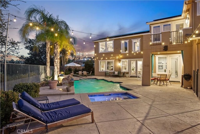 pool at dusk with a fenced in pool, fence, an in ground hot tub, french doors, and a patio area