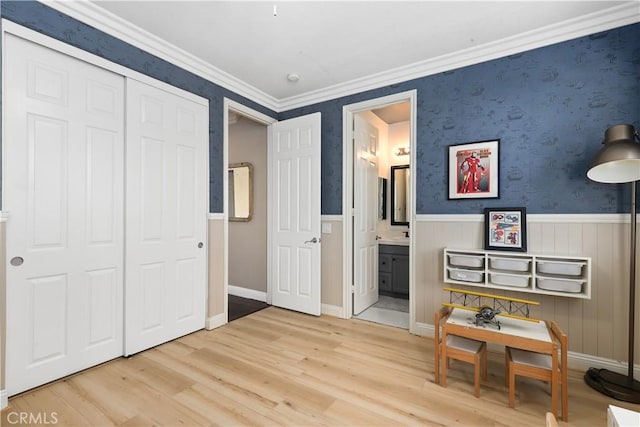 interior space featuring wood finished floors, baseboards, wallpapered walls, wainscoting, and crown molding